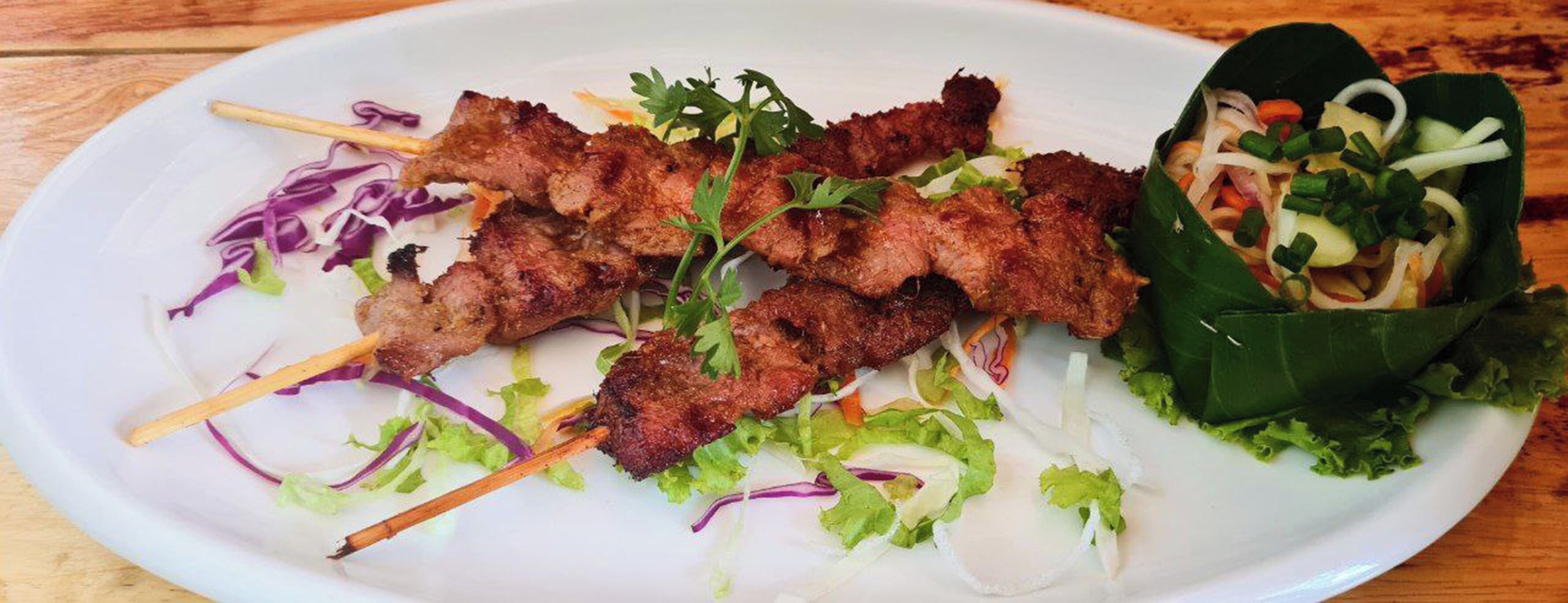 Une assiette de viande grillée en brochettes, accompagnée de légumes et d’une salade.