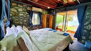 A bedroom with two beds, stone walls, wooden ceiling, and a view of the outdoors. - Europe Enchanted Bungalow Koh Rong (Koh Rong)