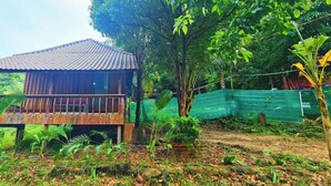 A wooden cabin with a balcony, surrounded by lush greenery and a green netting fence. - Europe Enchanted Bungalow Koh Rong (Koh Rong)