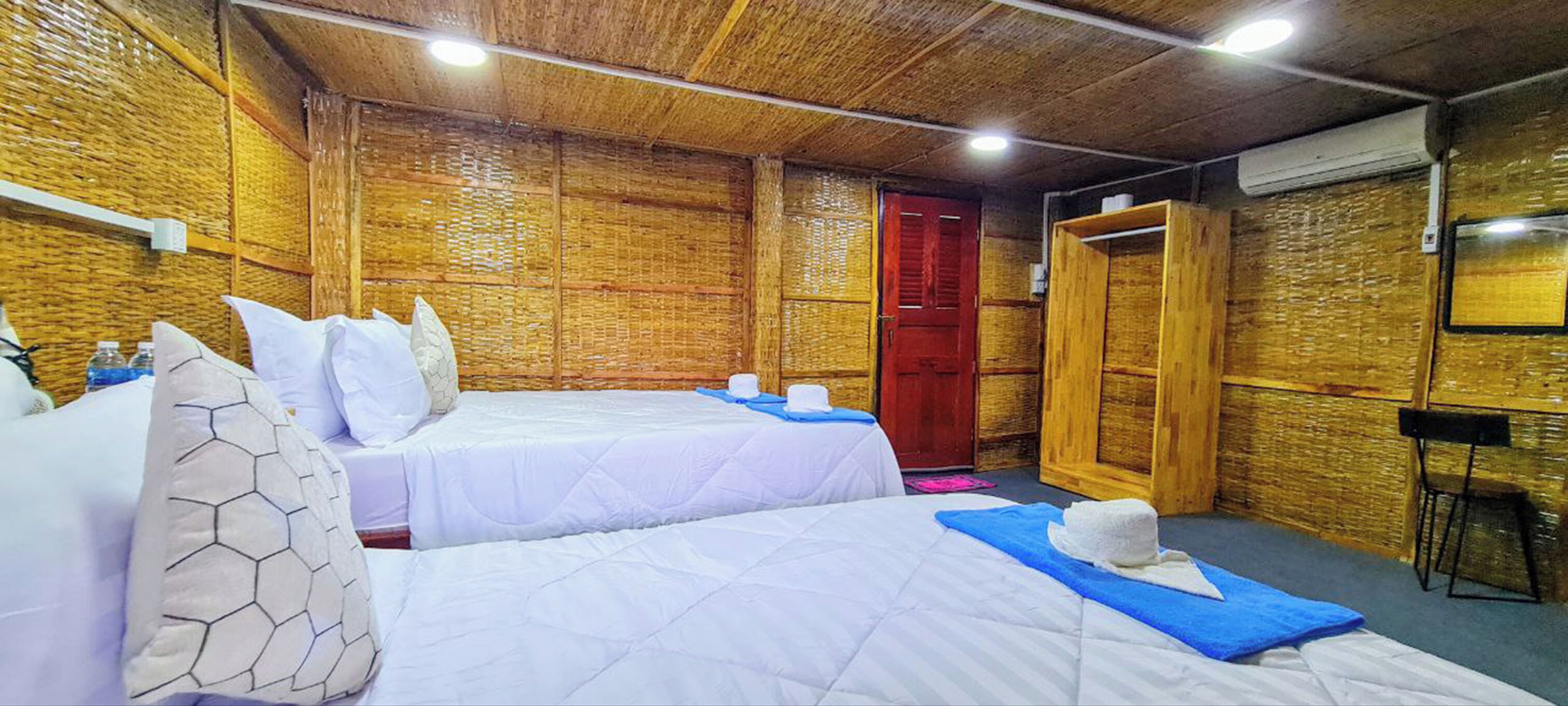 Une chambre avec deux lits, une porte en bois et une petite table avec une chaise.