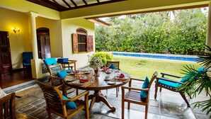Un patio coperto con un tavolo rotondo apparecchiato per mangiare, circondato da sedie in legno con cuscini blu.