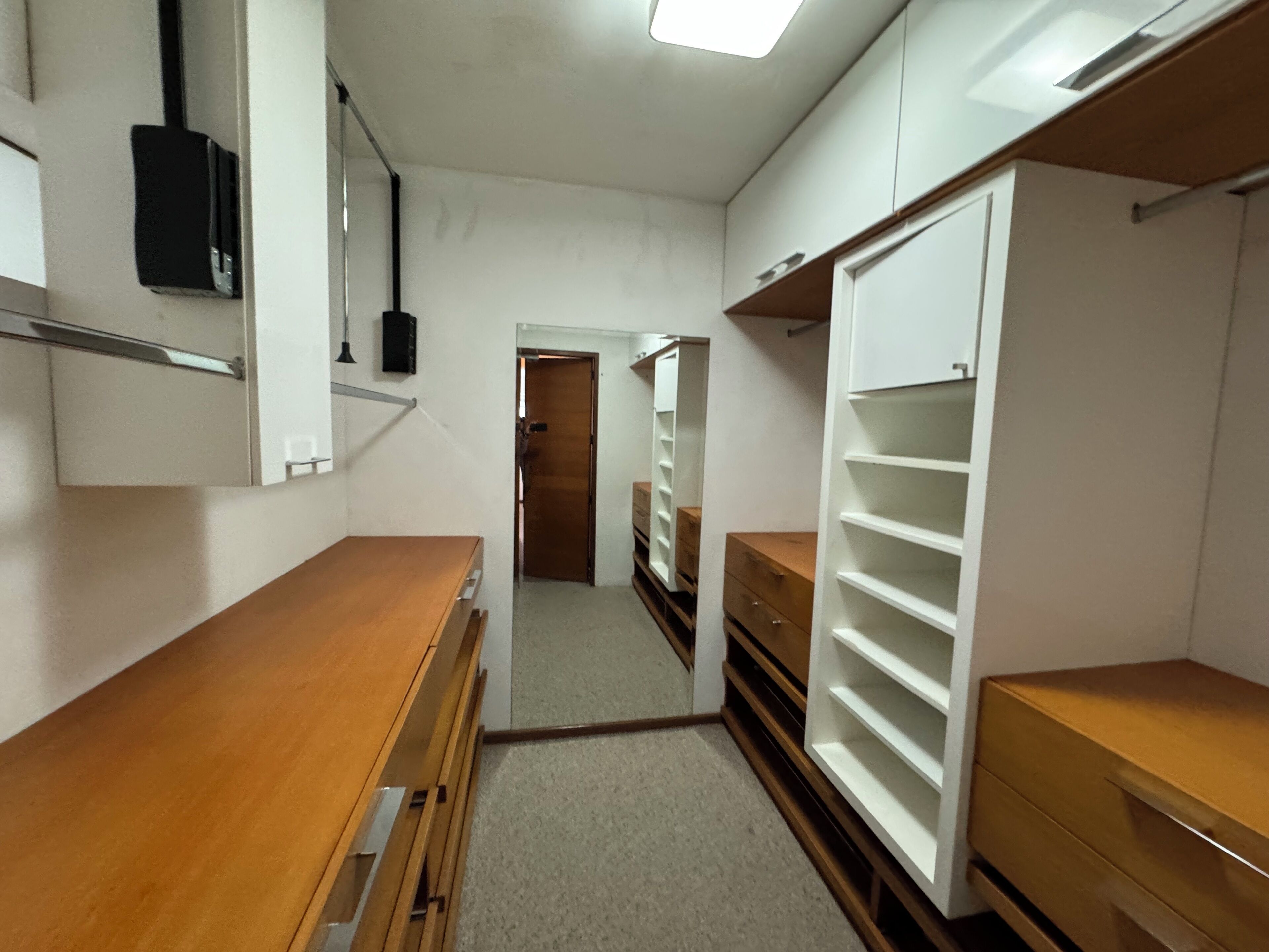 A narrow hallway with wooden benches and white shelving units.