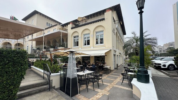 Un espace café en plein air avec des tables et des chaises, un lampadaire décoratif et un bâtiment doté d’un balcon.