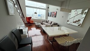 Un salon moderne comprenant un coin repas, une grande fenêtre donnant sur la ville et un escalier.