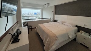 Une chambre d’hôtel moderne dotée d’un grand lit, d’un bureau avec un ordinateur et un téléphone, d’une chaise et d’un téléviseur fixé au mur.