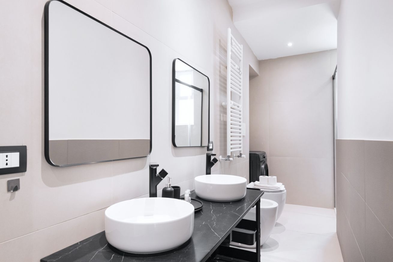 A modern bathroom with two round white sinks, a large mirror, and a towel rack.
