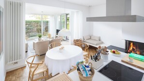 A modern living room with a round table, sofas, a fireplace, and a view of the outdoors. - // Pudelsand - Eins // (Norderney)