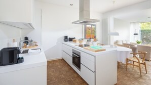 A modern kitchen with a central island, a built-in oven, and a large window. - // Pudelsand - Eins // (Norderney)