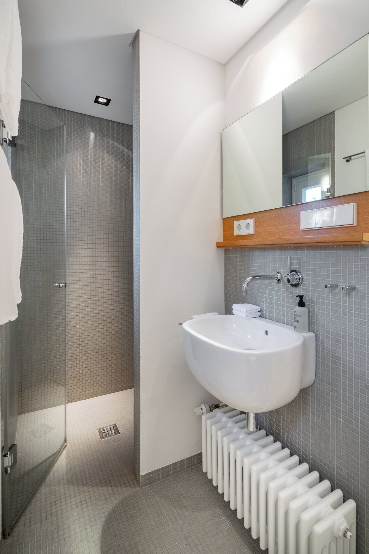 Ein modernes Badezimmer mit Duschkabine aus Glas, einem weißen Waschbecken mit Spiegel darüber und einem Heizkörper darunter.