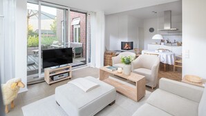 A modern living room with a flat-screen TV, a fireplace, and a dining area with a table and chairs. - // Pudelsand - Eins // (Norderney)
