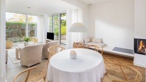 A modern living room with a round table, wooden chairs, a TV, and a fireplace. - // Pudelsand - Eins // (Norderney)