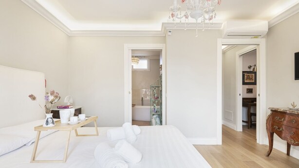 A hotel room with a large bed, a wooden bedside table with a vase and books, a chandelier, and a view of the bathroom. - Easylife - Sophisticated apartment with terrace (Milano)