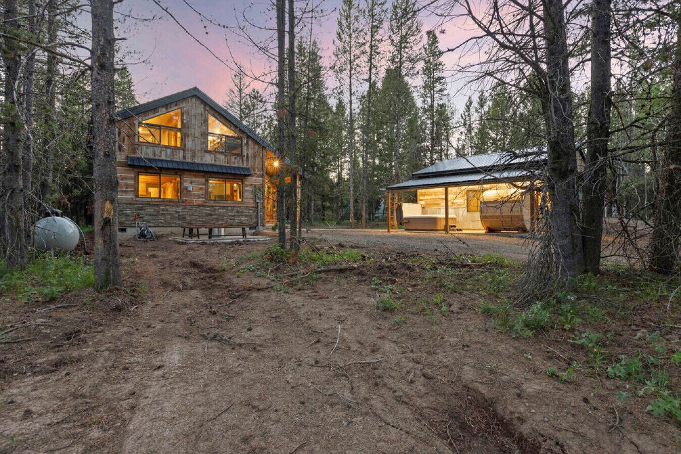 A rustic cabin with a large window and a covered porch, surrounded by trees.