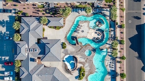 En vy från ovan över ett bostadsområde med en stor swimmingpool, flera avslappningsområden och en parkeringsplats.
