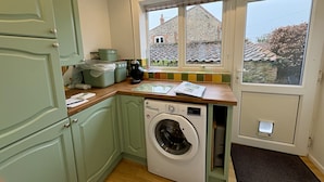 Une cuisine compacte équipée d’un lave-linge, d’une fenêtre donnant sur une maison et d’une porte avec un paillasson.