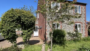 Un bâtiment en pierre de deux étages, avec une porte et des fenêtres blanches, entouré de verdure et d’un mur en pierre.