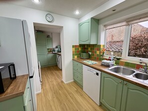 A kitchen with green cabinets, a dishwasher, a window with a view, and a clock on the wall.