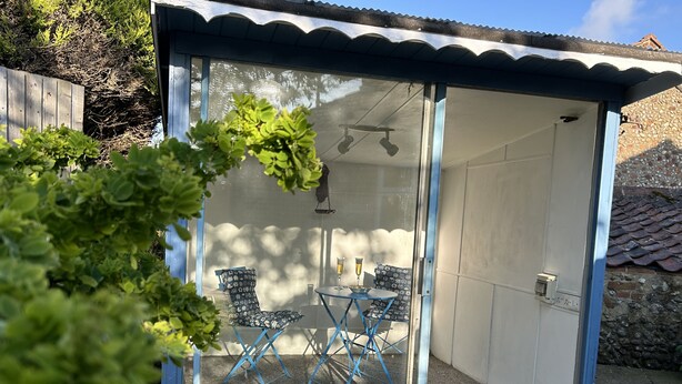 Une terrasse fermée par des baies vitrées, avec une table, des chaises, une porte et un petit tapis.