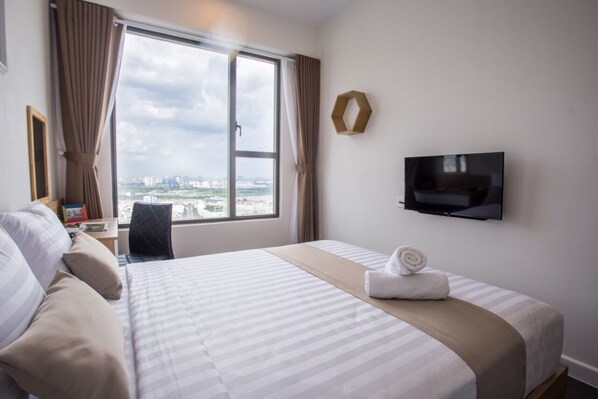 A hotel room with a large bed, a TV mounted on the wall, and a view of the city through a large window.