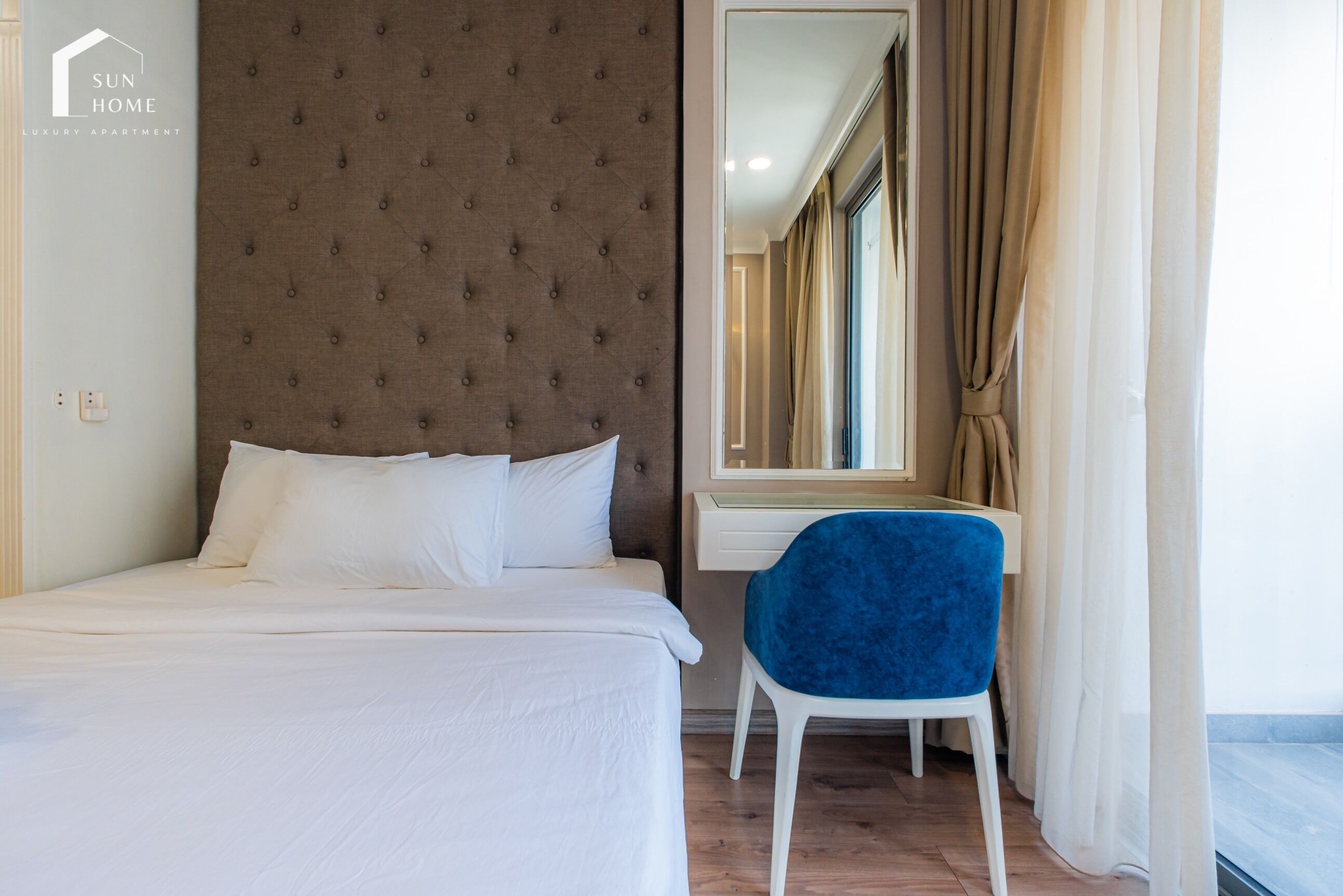 A bedroom with a bed, a blue chair, a large mirror, and a window with curtains.