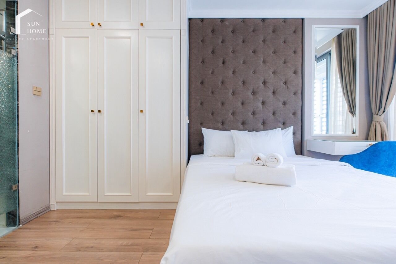 Un dormitorio con una cama grande, cabecera acolchada, armario blanco y zona de ducha con mampara de cristal.