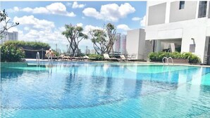 A swimming pool with lounge chairs and palm trees, surrounded by modern buildings. - River Gate Quan 4 Luxury Apartment (Ho Chi Minh City)