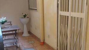 A narrow corridor with a tiled floor, a white pedestal with a plant, a metal table with a bench, and a decorative gate with a sign.