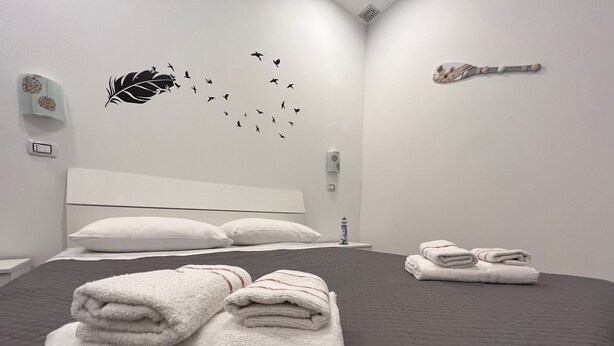 A neatly made bed with folded towels, a white headboard, and a wall decoration of birds flying.