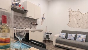 A modern kitchen with white cabinets, a dining table with a wine bottle and glass, and a grey sofa with patterned cushions.