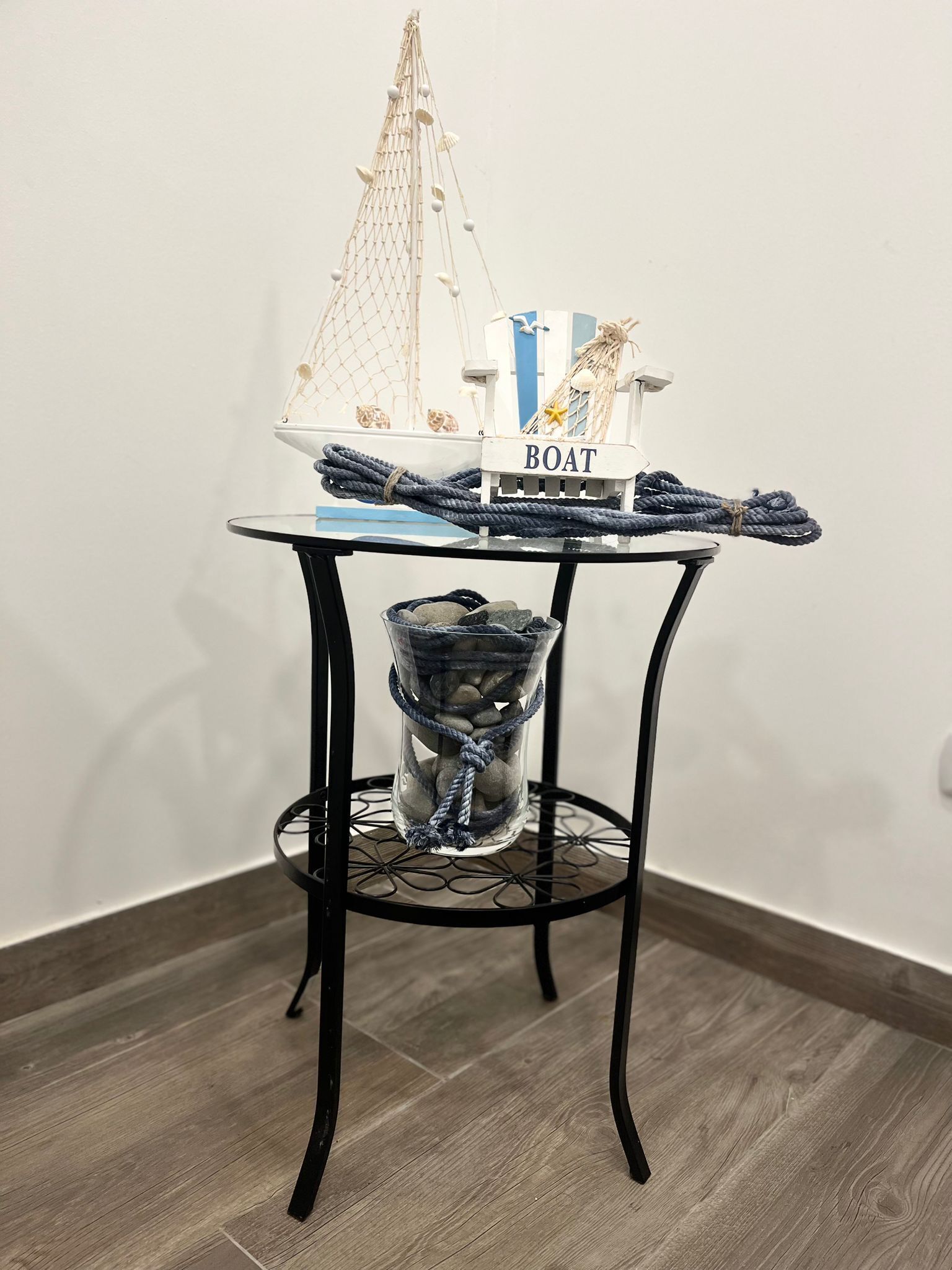 Una pequeña mesa con un modelo de velero, un cartel que dice "BOAT" y un recipiente de vidrio con cuerdas y piedras.