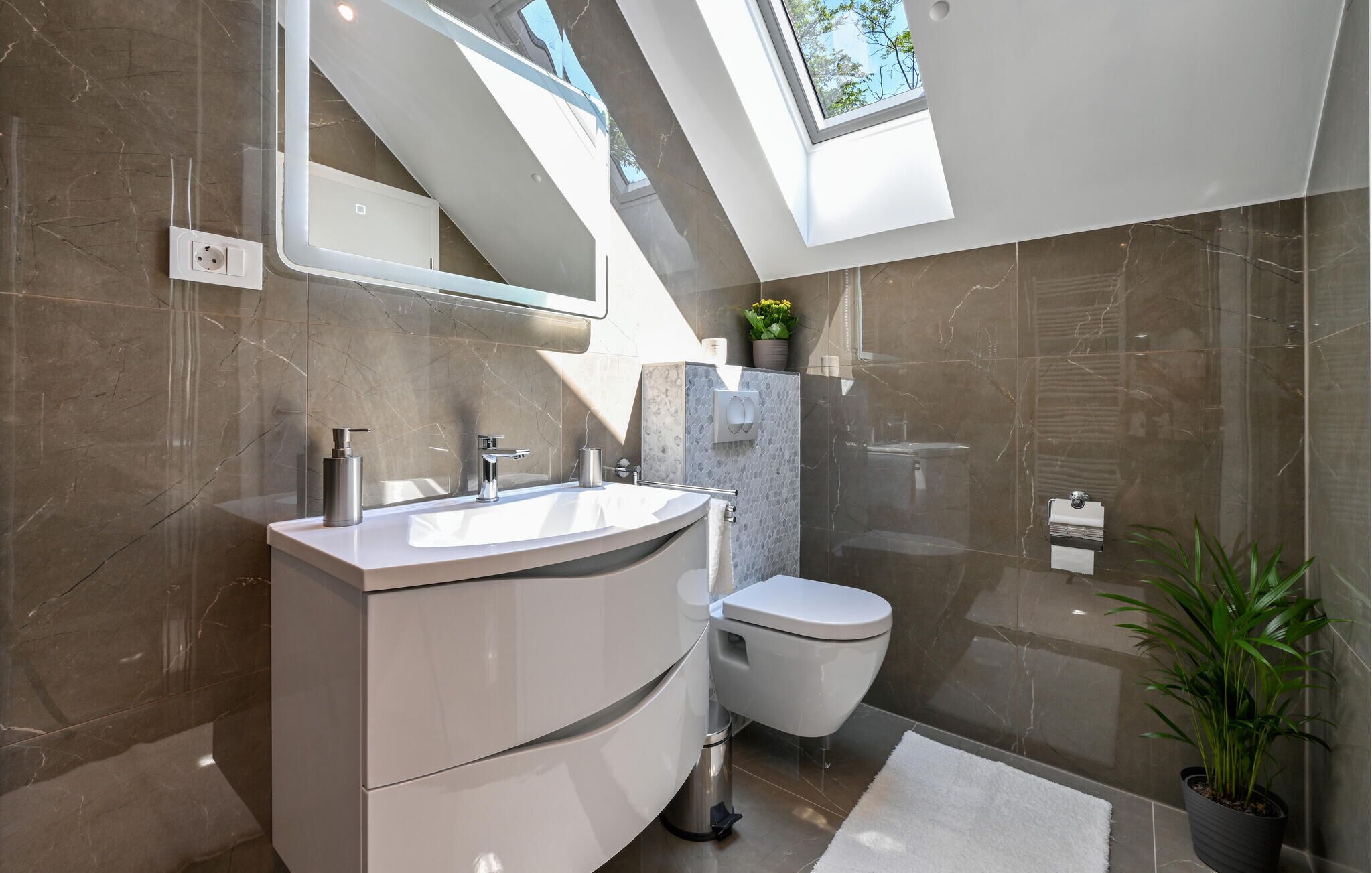 A modern bathroom with a skylight, a large vanity, a toilet, and a shower area.