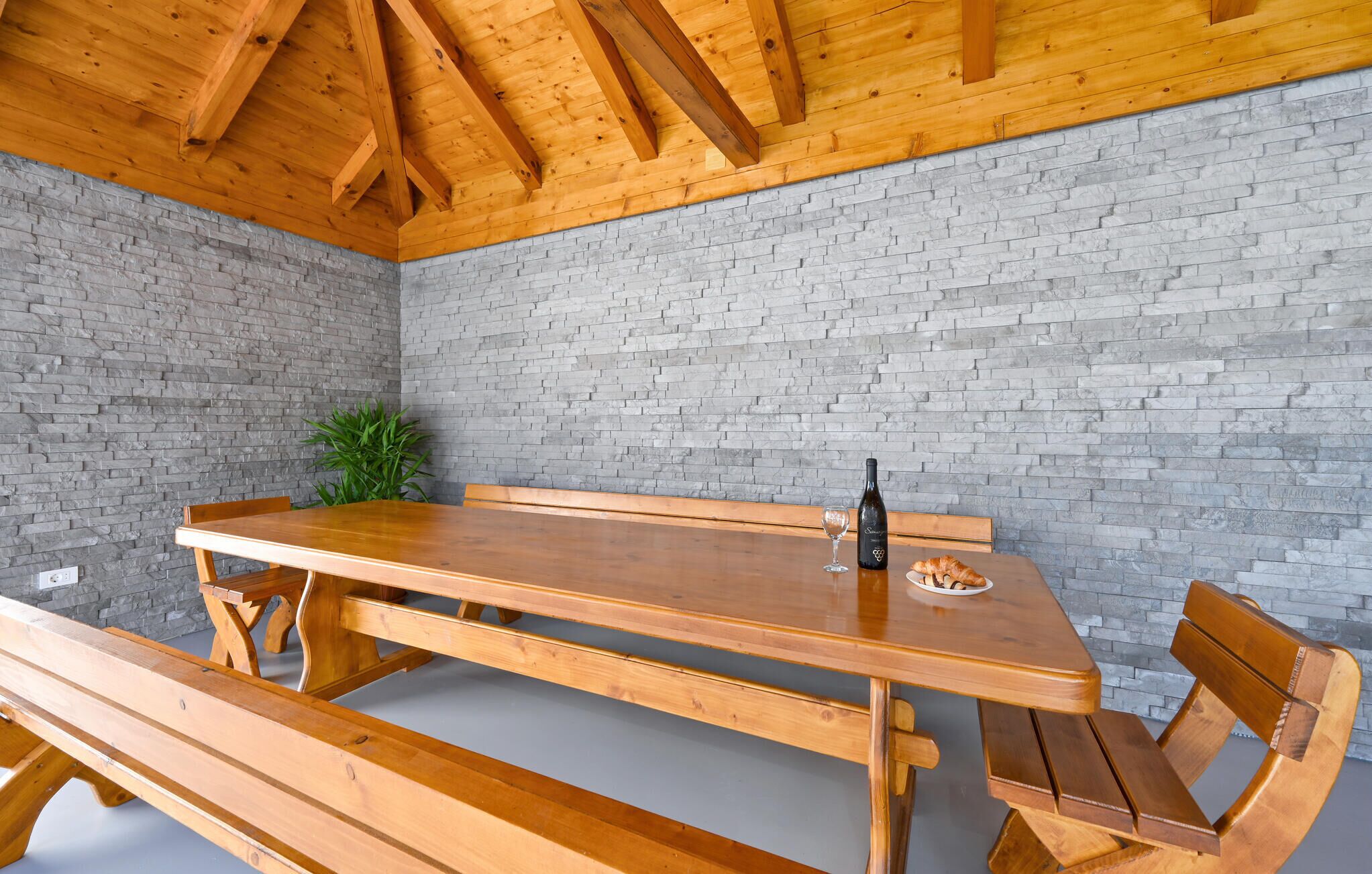 Een houten tafel met banken, een fles en een glas in een kamer met een bakstenen muur en houten balken aan het plafond.