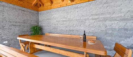 Een houten tafel met banken, een fles en een glas in een kamer met een bakstenen muur en houten balken aan het plafond.