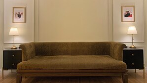 Une pièce dotée d’un grand canapé moelleux placé au centre, sur un plancher en bois, et flanquée de deux tables de chevet noires, sur lesquelles reposent des lampes et sont accrochées des photos encadrées.