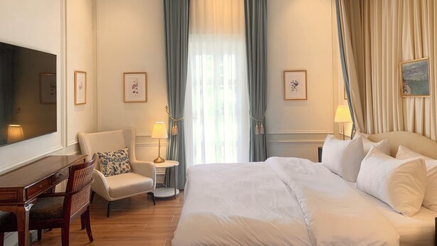 Une chambre d’hôtel avec un grand lit, un bureau, une chaise, une petite table avec une lampe et un téléviseur fixé au mur.