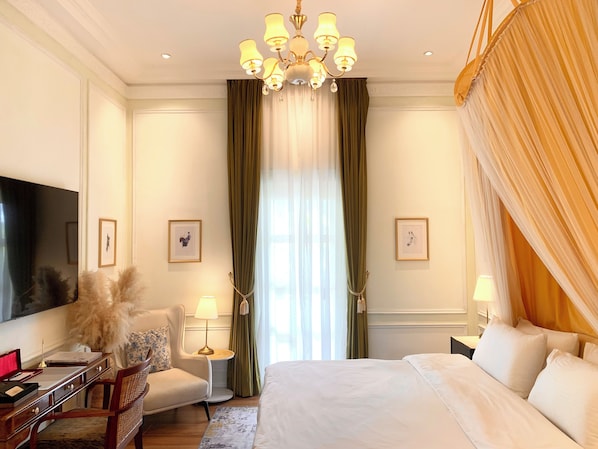 Habitación de hotel con una cama grande, un escritorio con lámpara, una silla, televisión y un candelabro.