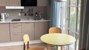 Une cuisine moderne équipée d’un four à micro-ondes, d’un évier et de placards. On y trouve une table à manger avec des chaises, ainsi qu’une fenêtre avec des rideaux.