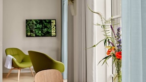 Una habitación moderna con una mesa redonda, una silla verde, una silla de madera, un jarrón con flores y un cuadro enmarcado en la pared.