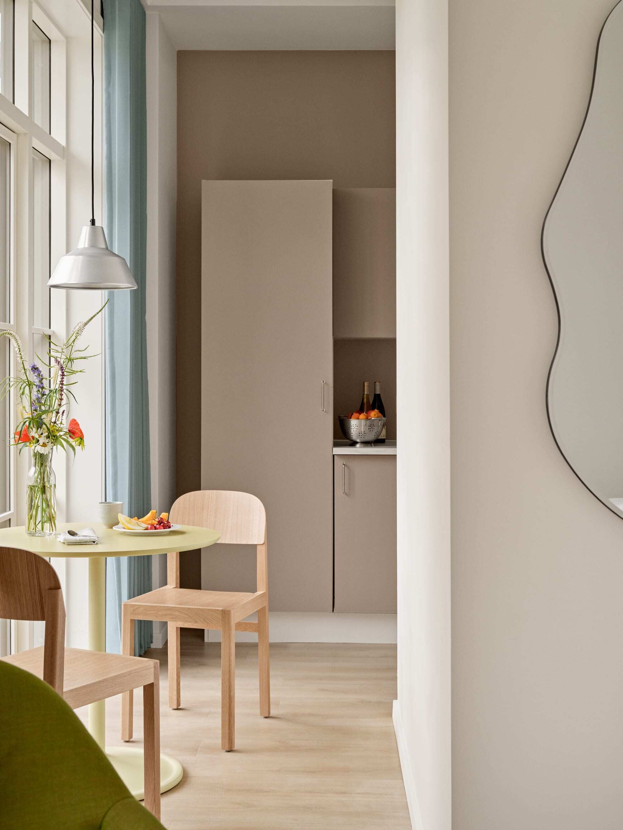 A modern kitchen with a round table, chairs, a hanging light, and a cabinet with bottles.