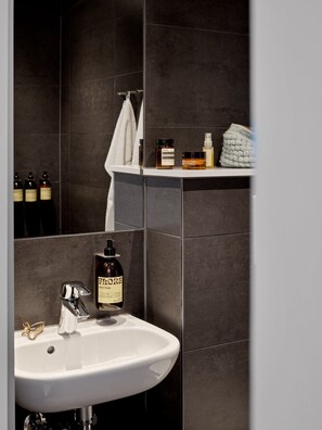 A bathroom with a white sink, dark tiles, and a shelf with toiletries.