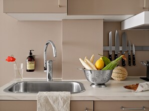A kitchen with a stainless steel sink, a colander with vegetables, a bottle of dish soap, and a knife block.