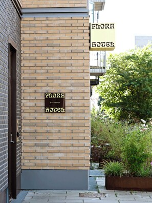 A hotel entrance with a brick facade and a sign indicating the name 'Flora Hotel'.