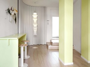 A modern hotel room with a light green desk and stools, a white curtain, and a sign indicating amenities like laundry and luggage.