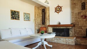 A living room with a white sofa, a round table with a plant, a fireplace, and two framed floral paintings on the wall.