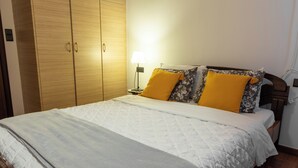 A neatly made bed with a white quilt and two pillows, one yellow and one with a floral pattern.