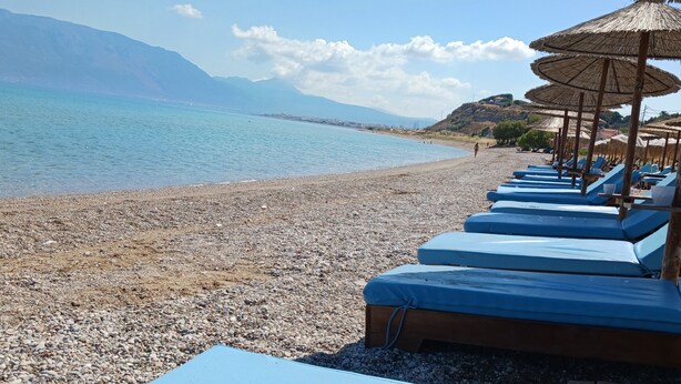 A beach with pebbled shore, lounge chairs, and thatched umbrellas.