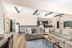 A spacious living area with a sectional sofa, a dining table, and a kitchen in the background.