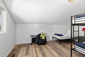 Un dormitorio con literas, una pequeña mesa redonda, un sillón de peluche y una ventana.