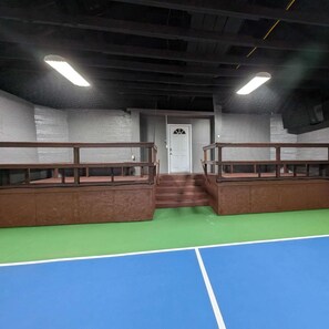 A sports court with a green and blue floor, wooden railings, and a white door in the background.