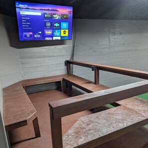 Ein Zimmer mit an der Wand montiertem Fernseher, der die Roku TV-Oberfläche anzeigt, einer Holzbank und einer kleinen Sitzecke.
